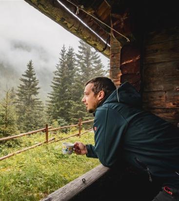 Ein Mann sieht aus einer Hütte in den nebeligen Wald.