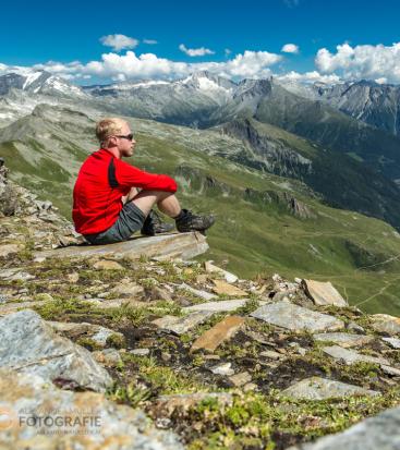 Ein Mann sitzt auf einem Berg und blickt in die Ferne.